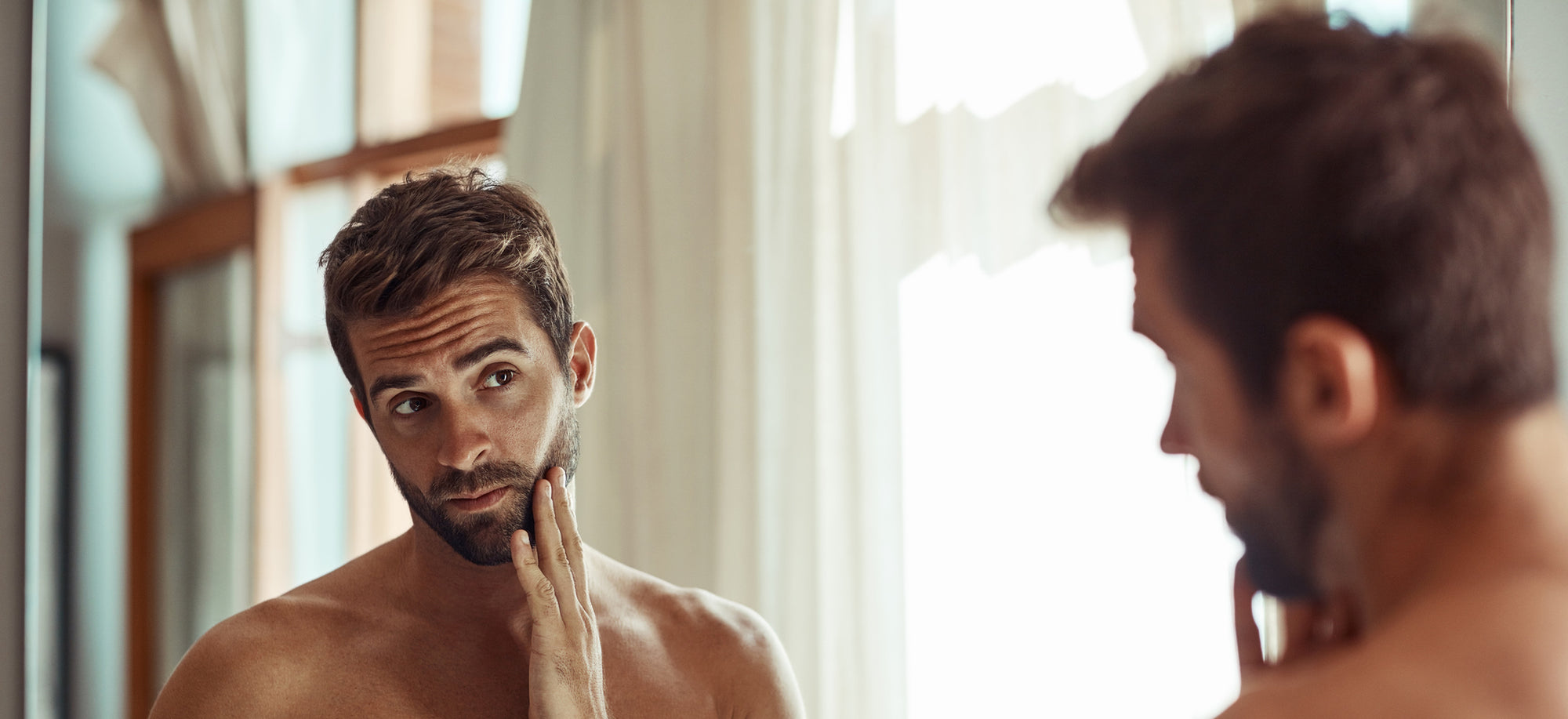 Handsome man in his 30's looking at his skin in the mirror