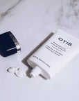 Tube of OTIS Protective Shave Cream open on marble surface with cream squeezed out and lid off