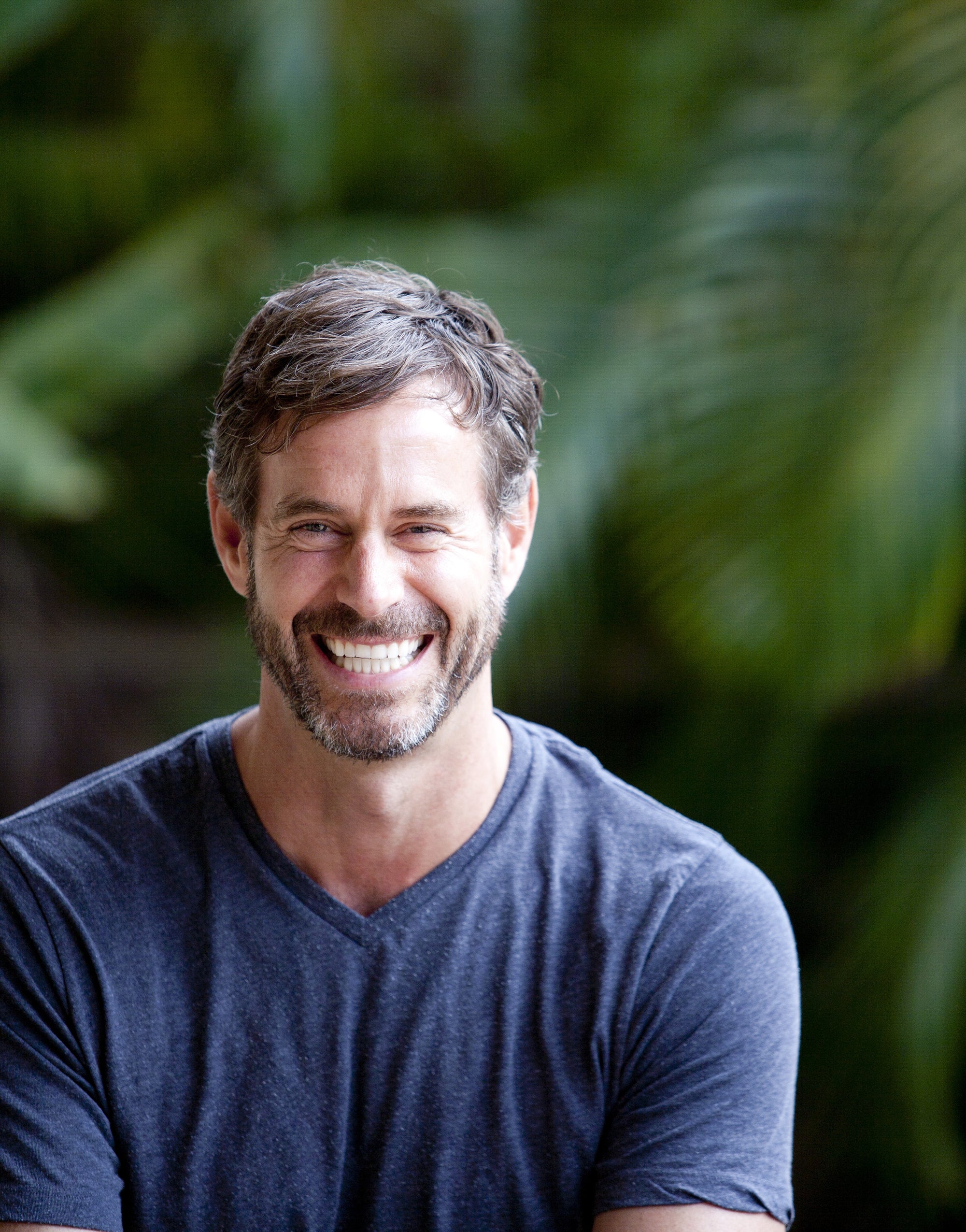 handsome man in his 40's smiling in front of green plants