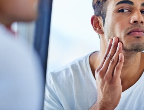 The Science of Men's Skin: How Hormones, Diet, and Stress Shape Your Complexion. Handome man looking in the mirror concerned about his skin
