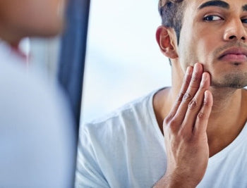 The Science of Men's Skin: How Hormones, Diet, and Stress Shape Your Complexion. Handome man looking in the mirror concerned about his skin