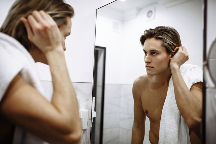 Young man looking in mirror to check his skin for acne scars