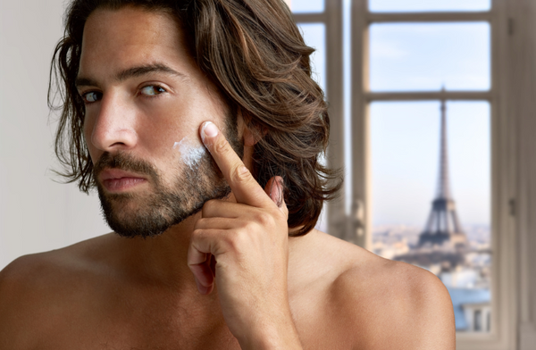 French man applying skincare with Eiffel tower, Paris outside window